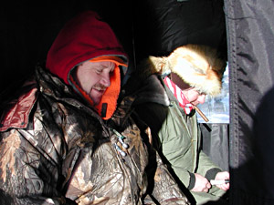 
Gary Feldmann (left) and Bill Zetchy (cigar and coonskin cap) watch the holes at their feet. The two men are from Wisconsin and are fishing Gull Lake for the first time. (MPR Photo/Jeff Horwich)