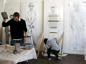 
A volunteer working clay to be thrown onto drawing, hanging behind, on wall.
 (MPR photo/Bob Kelleher)