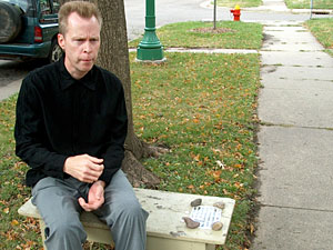 
Steve Heitzeg sitting on his bench memorial to Paul Wellstone. On the bench is a photograph of smiling Wellstone along with a Wellstone quote about social justice. (MPR Photo/ Mark Zdechlik)