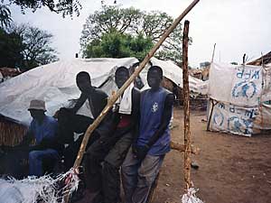 
The lean-tos which provide shelter for the refugees are visible behind this group of boys.  They are made from sticks and the plastic sheeting which is ripped from the United Nations food packages dropped by planes every few weeks.  (Photo by Doug McGill)