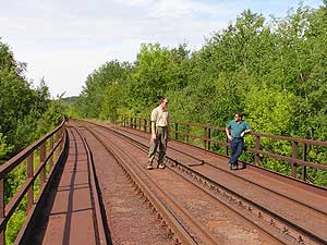 
Dave Lotti, right, and Bob Liebfried, left, walk the railroad bridge on the south side of the Canisteo Pit.  The rail line closed in February because of the danger tracks may fall into the expanding pit.  If the pit floods, it would most likely do so underneath this bridge. (MPR Photo/Bob Kelleher)