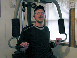 
Jim Vandenheuvel works out daily on a weight machine in his family's living room.  He's adds the weight training to speech and physical therapy he receives at the Minneapolis VA hospital.  (MPR Photo/Tim Post)