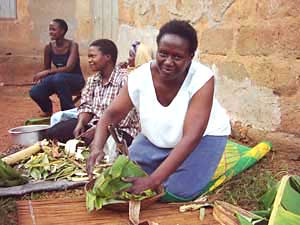 
Sarah Kalema prepares matooke, a traditional Ugandan dish of mashed plaintains steamed inside banana leaves, as translator and guide Gloria Birungi crouches and looks on. (Photo: Jonah Eller-Isaacs)