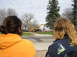 
Two women watch the destruction of a former meth house in Sacred Heart from across the street.  Both said everyone in town knew the residents of the house were making meth.   (MPR Photo/Tim Post)