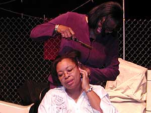 
A hot comb demonstration, courtesy of Shonda Allen (seated) and Nede Williams (standing). Allen shows how when she was a girl she used to pull down her ear to protect it from getting burned. (MPR photo/Chris Roberts)